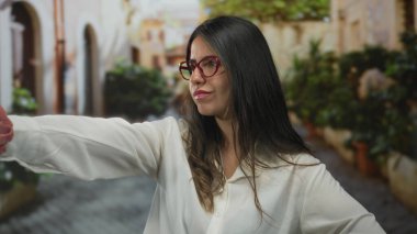 Gözlüklü, beyaz tişörtlü, yeşil tişörtlü, etkileyici bir caddeyi işaret eden bir kadın, açık havada azim ve kararlılık gösteriyor..