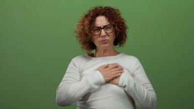 Göğsü sıkışan, yeşil duvara yaslanmış, gözlüklü ve beyaz gömlekli bir kadın.