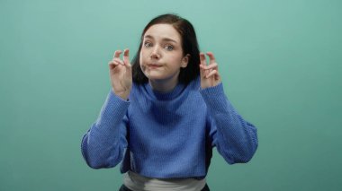 Mavi süveter giymiş, yeşil arka planda hareket eden ve elleri rahat bir şekilde vurgu yapan bir kadın..