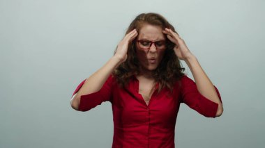 Kırmızı gömlekli ve gözlüklü bir kadın stresli görünüyor, iki eliyle başını izole edilmiş beyaz bir arka plana doğru tutuyor.