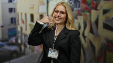 Şehir sokağında bana işaret veren bir kadın, sarı saç ve gözlüklü, canlı şehir atmosferinde iş kıyafetlerini renklendiren, duvar yazısı binalarıyla çevrili bir kadın..