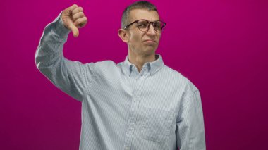 Gözlüklü beyaz bir adam canlı pembe izole bir duvara başparmak hareketi yapıyor. Çizgili gömlek giyiyor. Onaylamadığını ve ciddiyetini gösteriyor..