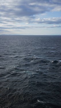 Parçalı bulutlu bir gökyüzünün altında dalgalı dalgalarla genişleyen okyanus, ufukta dinamik ama dinamik bir deniz manzarası olduğunu gösteriyor..