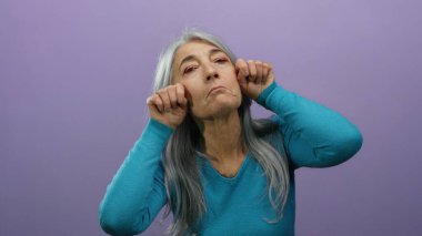 Üzüntüsünü ifade eden bir kadın, mor bir arka plana karşı yüz ifadeleri kullanırken, son sınıfların duygularını ve gri saçlarını samimi bir şekilde gösteriyor..