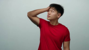 Kırmızı gömlekli genç adam, beyaz arka plan duvarına karşı çeşitli düşünceli ifadeler sergiliyor..