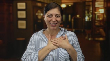 Çizgili gömlekli orta yaşlı kadın, inşaat girişinde göğsüne sıcak ışık altında dokunuyor..