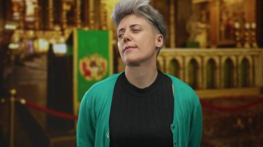 Gümüş saçlı bir kadın kilise sunağının önünde yüzünü gösteriyor. Sıcak ışık altında yeşil bir bez ile örtülmüş..