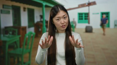 Açık hava kahve restoranının terasında el kol hareketi yapan arka planda sokak manzaralı sakin şehir manzarası olan bir kadın..