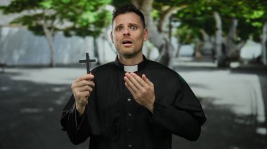 Şehir caddesinde karşıdan karşıya geçen adam siyah dini giysiler giymiş canlı yeşil doğa ve kentsel altyapının arasında umut ve inanç ifadesiyle yukarı bakıyor..