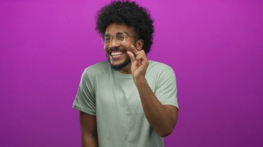 Afro-Amerikan bir adam parmaklarıyla küçük bir jest yapıyor canlı pembe arka plana karşı, mizah ve oyunculuk taşıyor anlamlı bir gülümsemesi ve kıvırcık saçlarıyla.