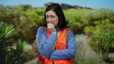 Yeşil bir parkta, arka planda ağaçlar olan turuncu yelek giyen gönüllü bir kadın..