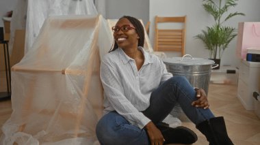 Yeni bir evde kutlayan bir kadın. Paketleri açılmış bir şekilde yerde oturuyor. Oturma odasında heyecanını ve neşesini dile getiriyor..