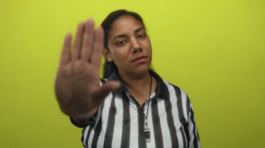 Siyah-beyaz çizgili gömlek giyen kadın hakem, stüdyoda limon yeşili duvarı olan jesti durdurmak için avuç içini ileri atıyor..