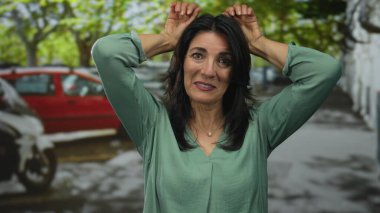 İspanyol orta yaşlı kadın gülümser ve tavşan kulaklı el kaldırır şehir caddesinde jest, neşeli eğlence kaprisli.