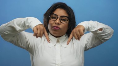 Kendinden emin bir ifadeyle aşağıya bakan, mavi arka planda gözlüklü ve beyaz gömlekli bir kadın, güçlendirilmiş bir Latin kimliği tasvir ediyor..