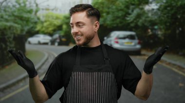 Önlük ve siyah eldiven giyen genç adam park etmiş arabalarla bir caddede gülümseyerek bir garson ya da sokak satıcısı havası yaratıyor..