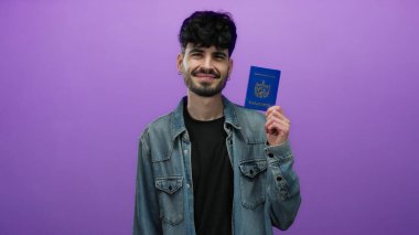 İzole edilmiş mor duvara karşı Küba pasaportu tutan, sıradan kot giyimli, modern keşif ruhunu temsil eden, kimlik ve seyahat temaları sergileyen bir adam..