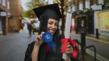 Mezuniyet kepi ve cüppeli genç İspanyol kadın gururla elinde diploma ve mavi kurdele ile şehir caddesinde duruyor..