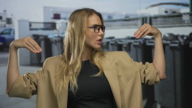 Bir şehir caddesinde, gözlüklü ve şık bej ceketli bir kadın açık hava kentsel ortamında canlı bir mesaj iletiyor..