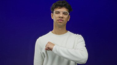 Uzun kollu kurdeleli gömlek giyen gümüş çerçeveli gözlüklü adam stüdyoda ileri doğru sıkılmış bir yumruk gösteriyor..