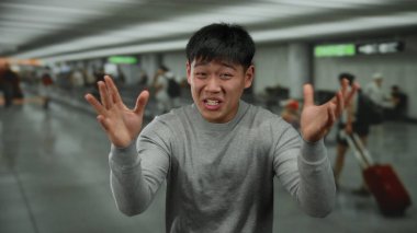 Havaalanı terminalinde hayal kırıklığını ifade eden genç bir adam. Etrafı bulanık yolcularla çevrili. Seyahat stresi ve yoğun bir ev ortamını aktarıyor..