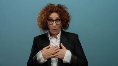 Mavi arka planda kıvırcık saçlı, iş elbisesiyle sürpriz yapan bir kadın..