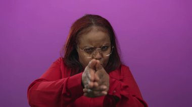 Kadın ellerini göğüs hizasında parlak mor stüdyo ışıkları altında tabanca jestine dönüştürüyor..