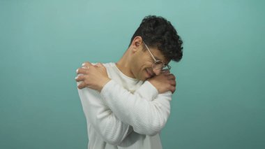 Gözlüklü ve beyaz süveter giyen İspanyol genç adam stüdyoda omuzlarına sarılıyor..