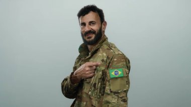 Askeri üniformalı İspanyol adam kolunda Brezilya bayrağı olduğunu gösteriyor. Gri bir arkaplanda gururlu bir ifade ve sakalla duruyor..