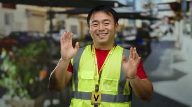 Yansıtıcı yelek giymiş gülümseyen adam canlı bir şehir arka planında binalar ve yeşilliklerle gönüllü oluyor..