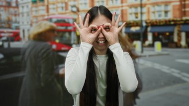 Arka planda ikonik kırmızı otobüslerle gülümseyen kadın şehir ortamında neşeli bir ifade ve neşe sergiliyor.