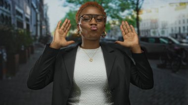 Gözlüklü ve siyah ceketli bir kadın, şehir caddesinde park etmiş arabalar ve bisikletlerle el ele tutuşuyor..