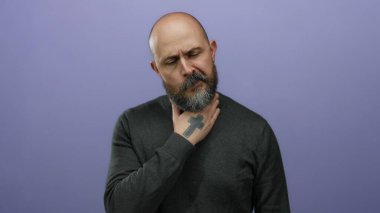 Sakallı ve dövmeli bir adam, izole edilmiş mor arka planda boğaz ağrısı çekiyor. Yakın plan çekimde rahatsızlık veriyor..