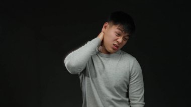 Gri kazaklı genç Çinli adam siyah bir arkaplan karşısında duruyor. Acı dolu bir ifadeyle kafasına dokunmaktan rahatsız olduğunu ifade ediyor..