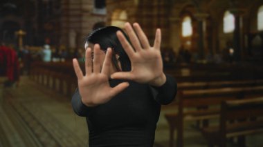 Kadın kilisedeki ayin sırasında durmak için elini kaldırıyor. Endişeli bir anda içeride gözlük takan Latin bir genç tapınmacıyı yakalıyor..