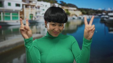 Resimli bir sahil kenarında rıhtımdaki teknelerin yanında el hareketleriyle şüphecilik gösteren genç bir kadın..