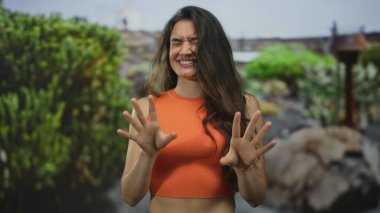 Kadın yüzü buruşur ve kollarını kaldırır ve parmakları orman yeşilliğinde parlak güneş ışığı altında yayılır; iğrenme.