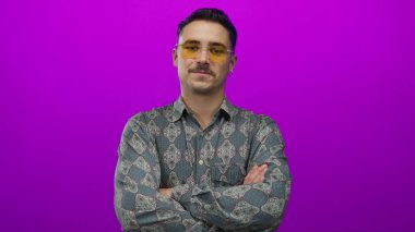 Genç adam kollarını kavuşturarak poz veriyor, parlak pembe arka plana karşı desenli gömlek giyiyor, stüdyo ortamında modern tarz ve hareketli tavırlar sergiliyor.