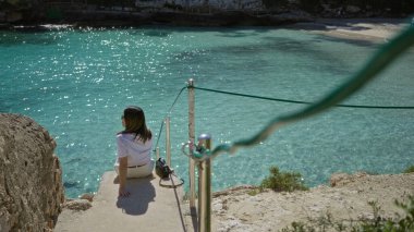 Mallorca 'daki Cala Llombards plajında turkuaz denizde dinlenen, çarpıcı Akdeniz manzarasına bakan, parlak güneş ışığı altında huzurlu tatil anlarının tadını çıkaran bir kadın..