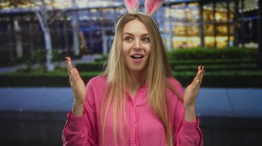 Pembe tişörtlü tavşan kulaklı kadın Paskalya kutlamaları sırasında şehir binasının önünde sürpriz yapıyor.