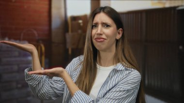 Çizgili gömlekli genç İspanyol kadın inşaat halindeyken inşaat halindeyken avuçlarını kaldırıyor; belirsizlik içinde..