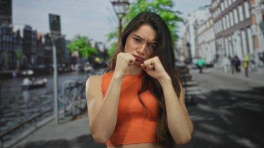 Arkasındaki dar binalar ve kanallı teknelerle günışığı sokağında yumruk kaldıran kadın, kararlılık..