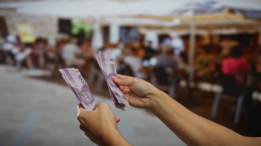 Endonezya rupiasını arka planda bulanık bir restoranla birlikte açık bir şehir ortamında tutan eller para değişimi içeren ticari işlemleri gösteriyor..