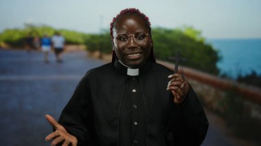 Rahip kılığındaki kadın deniz kenarındaki güvertede karşıdan karşıya geçiyor. Huzurlu sahil düzenine karşı ruhaniliği ve huzuru çağrıştırıyor..