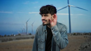 Bir tarlada el pençe divan duran genç adam mavi gökyüzünün altında yel değirmenlerinin önünde duruyor. Kot ceket giymiş, doğa enerjisini ve merakını gözler önüne seriyor..
