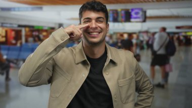 Adam parmaklarını burnuna yakın tutuyor ve havaalanının içinde dokunuyor. İspanyol bir genç, terminal tahtasının yanında durup nazikçe gülümsüyor..