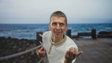 Sahilde gitar çalarken neşeli bir şekilde taklit eden bir adam, sakin plaj ve deniz müziğini güneşli bir açık havada dinlendirici bir zemin olarak hisseder..