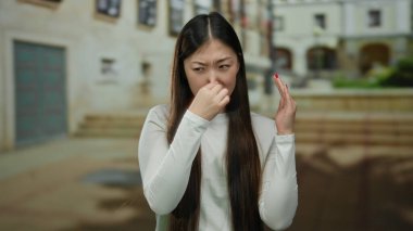 Şehir merkezinde beyaz gömlek giyen bir kadın binanın arka planındaki bulanıklığa karşı rahatsızlığını dile getiriyor..