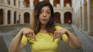 Kadın parmağı, tarihi üniversite binası kemerlerinin ortasındaki sarı gömleğini aşağı doğru işaret ediyor..