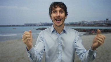 Açık mavi gömlekli bir adam, deniz kenarındaki kumlu bir sahilde elleri olan gözleri kapatır. Sürpriz..